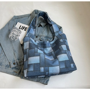 Flat lay of a large blue patchwork denim tote bag with wide straps and lifestyle props