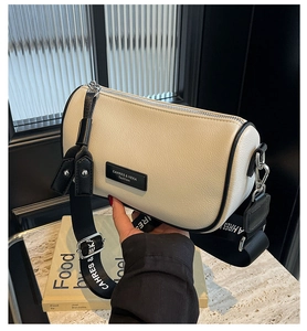 Detail of cream white leather pillow bag with wide black strap and silver metallic hardware