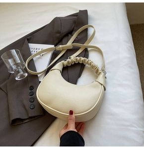 Close-up of beige lychee texture leather dumpling bag with ruched handle and silver hardware
