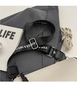 Detail view of cream pillow bag with wide branded textile strap and slim leather strap