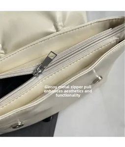Détail du curseur de fermeture éclair en métal argenté poli sur un sac plissé crème