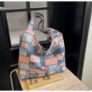 Detail of patchwork hobo bag with denim texture and floral patterns on stone pedestal
