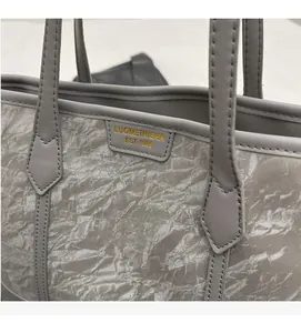 Close-up of textured grey tote bag featuring metallic finish and gold brand leather tag