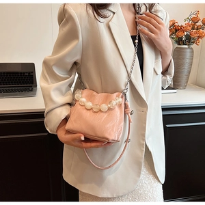 Detail of pink pleated crossbody bag with pearl handle worn with beige blazer