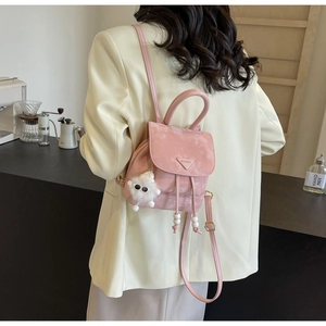 Pink mini backpack detail with triangular logo and white plush ball charm shown on shoulder