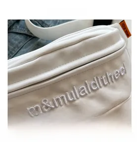 Macro detail of white fabric chest bag showing premium 3D letter embroidery and zipper