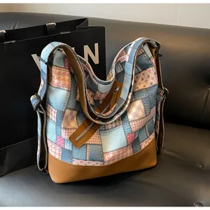 Detail of a large denim patchwork tote bag with brown leather base and side zippers