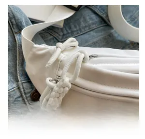 Detail of white nylon chest bag featuring thick knot zipper pulls and embroidery