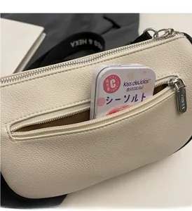 Close-up of white grained leather crossbody bag showing front zipper pocket and texture