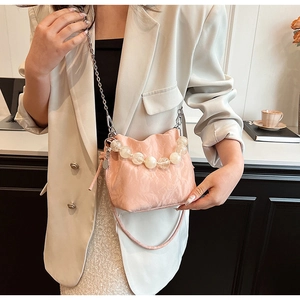 Detail of pink pleated bucket bag featuring large translucent bead handle and chain strap