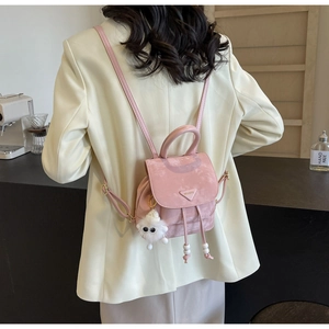 Back view of a mini pink backpack with a plush charm on a model in white blazer