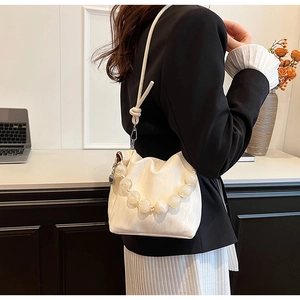 Detail of beaded handle and knotted strap on a white pleated bucket bag with shiny finish