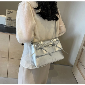 Sac à bandoulière argenté plissé avec détails de nœuds porté par un mannequin