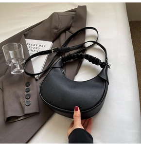 Detail of black dumpling bag with lychee pattern leather and pleated handle on grey blazer