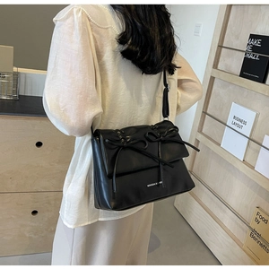 Détail d'un sac bandoulière noir plissé avec double nœuds décoratifs et finition en similicuir
