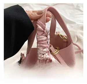 Close-up of pink lychee leather bucket bag featuring silk scarf handle and gold hardware