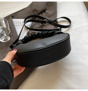 Detail view of black pebble leather croissant bag with pleated handle and silver hardware