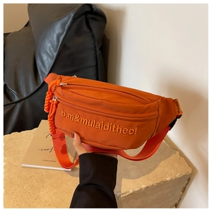 Detail of orange canvas belt bag featuring embroidered letters and adjustable strap