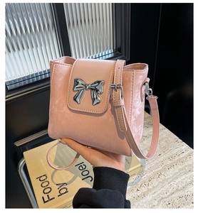 Pink bucket bag with silver metal bow detail and fine texture held in hand