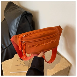 Detail of orange canvas crossbody bag featuring white letter embroidery and a textured strap