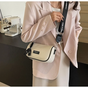 Close-up of beige leather cylinder bag featuring a black and white lettered webbing strap
