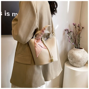 Detail of beige lychee leather bucket bag featuring a silk scarf handle and gold padlock