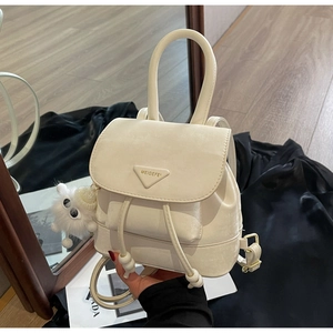 Close-up of cream mini backpack with triangular logo, drawstring and plush charm