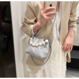 Close-up of grey pleated bucket bag with marble bead handle and metal chain strap