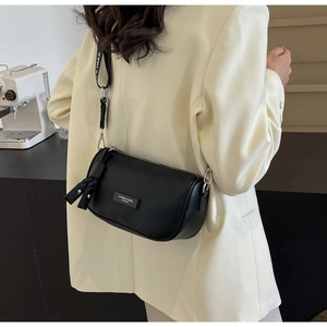 Detailed view of black cylindrical pillow bag with wide letter-print strap on model