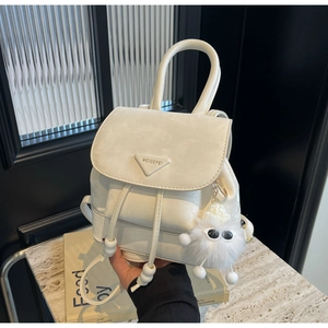 Detailed close-up of cream-white leather backpack with drawstring and plush charm