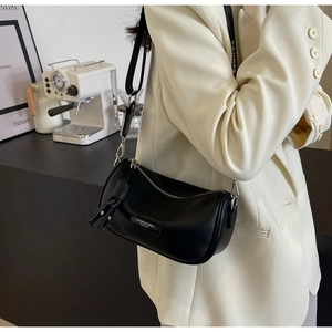 Detail of black leather cylinder bag with tassel zipper and metal logo plate on shoulder