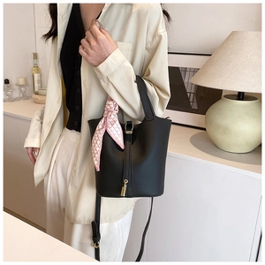 Close-up of black lychee leather bucket bag with gold padlock and pink silk scarf