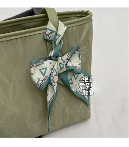 Close-up of sage green tote bag featuring textured pleats and decorative fashion silk scarf