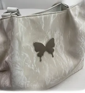 Detailed macro view of a silver butterfly metallic hardware on a white wrinkled leather tote