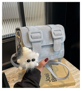 Detail of light blue crossbody bag featuring matte texture and a white fuzzy monster charm