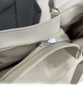 Detailed close-up of smooth silver metal zipper and neat stitching on a white leather tote