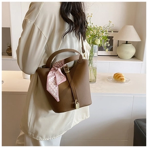 Brown lychee leather bucket bag with silk scarf detail shown in elegant lifestyle setting