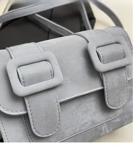 Close-up of grey-blue crossbody bag featuring dual buckle flap and matte finish texture
