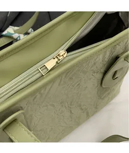 Detail showing smooth golden metal zipper and wrinkled texture on light green tote bag