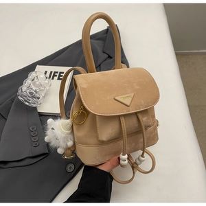 Detailed close-up of a khaki suede mini backpack with plush pom-pom and drawstring