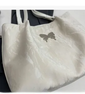 Detail of glossy wrinkled texture and silver butterfly metal hardware on white tote bag