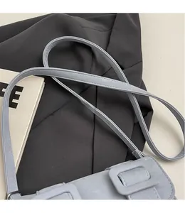 Detail of light blue matte leather crossbody bag with a square buckle on a grey background