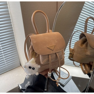 Detail of beige mini backpack with triangle logo, drawstring, and plush monster charm