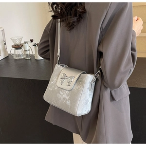 Silver bucket bag with metallic texture and bow detail worn by a model in a modern setting