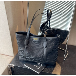 Detail shot of black tote bag featuring unique pleated texture and woven brand label