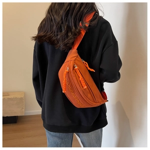 Detail of caramel orange canvas crossbody bag with letter design worn by model