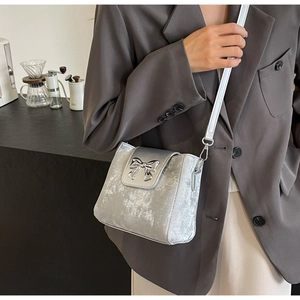Close-up of a silver bucket bag featuring a metallic bow detail and white leather strap