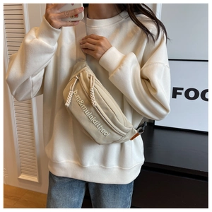 Detail view of beige nylon crossbody bag featuring letter embroidery and woven zipper pull