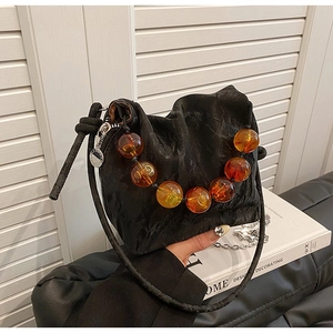 Detail of beaded handle with amber translucent pearls on a black wrinkled fabric bag