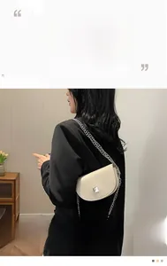 Close-up of cream-colored saddle bag with silver chain strap and metal buckle detail